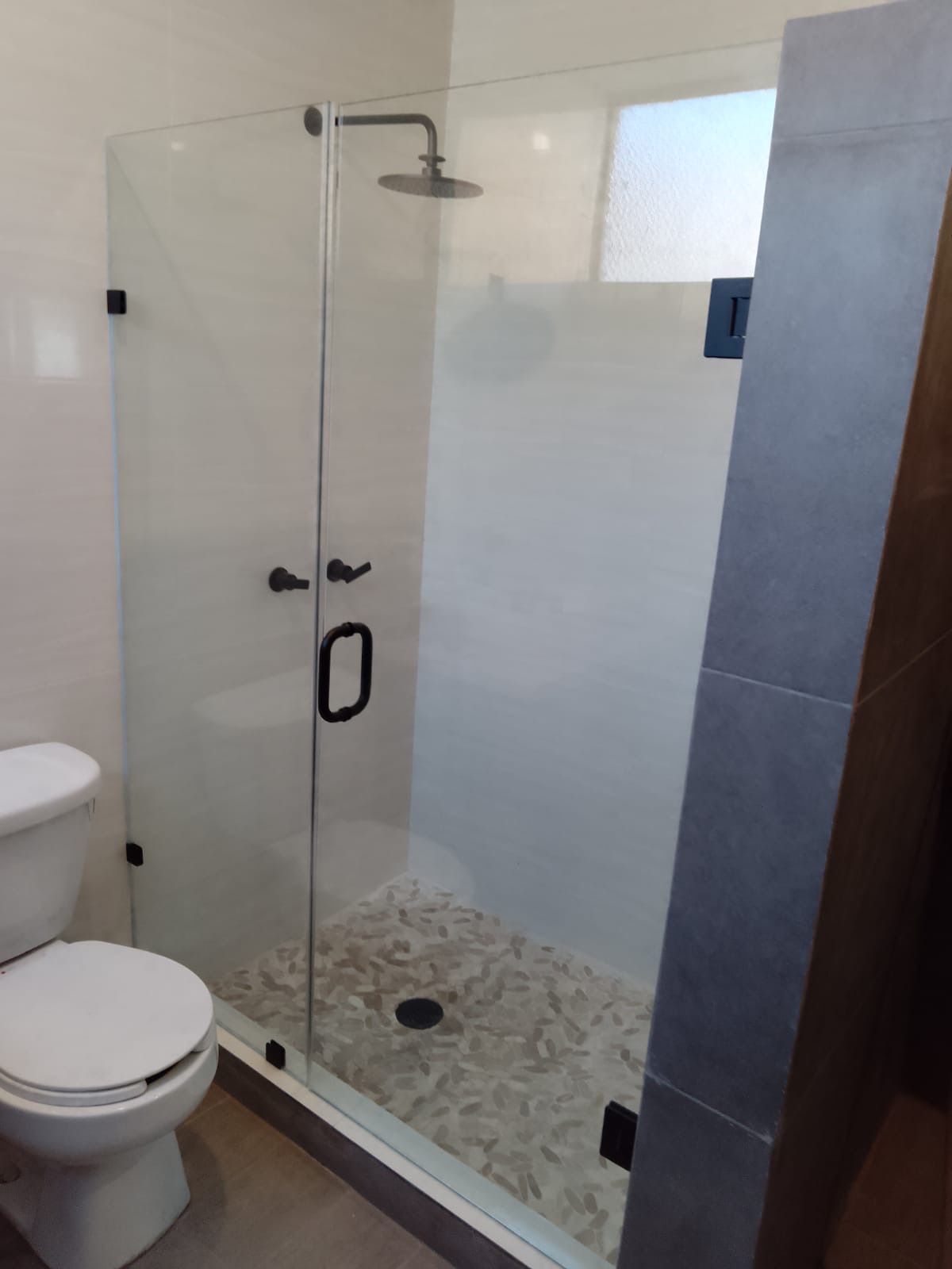 Cancel de baño abatible con panel fijo y herrajes negro mate en una residencia de Querétaro