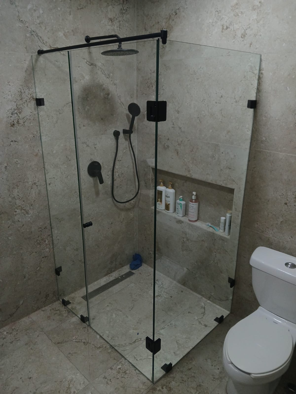 Herrajes negro mate en un cancel abatible armado a escuadra, en baño de travertino